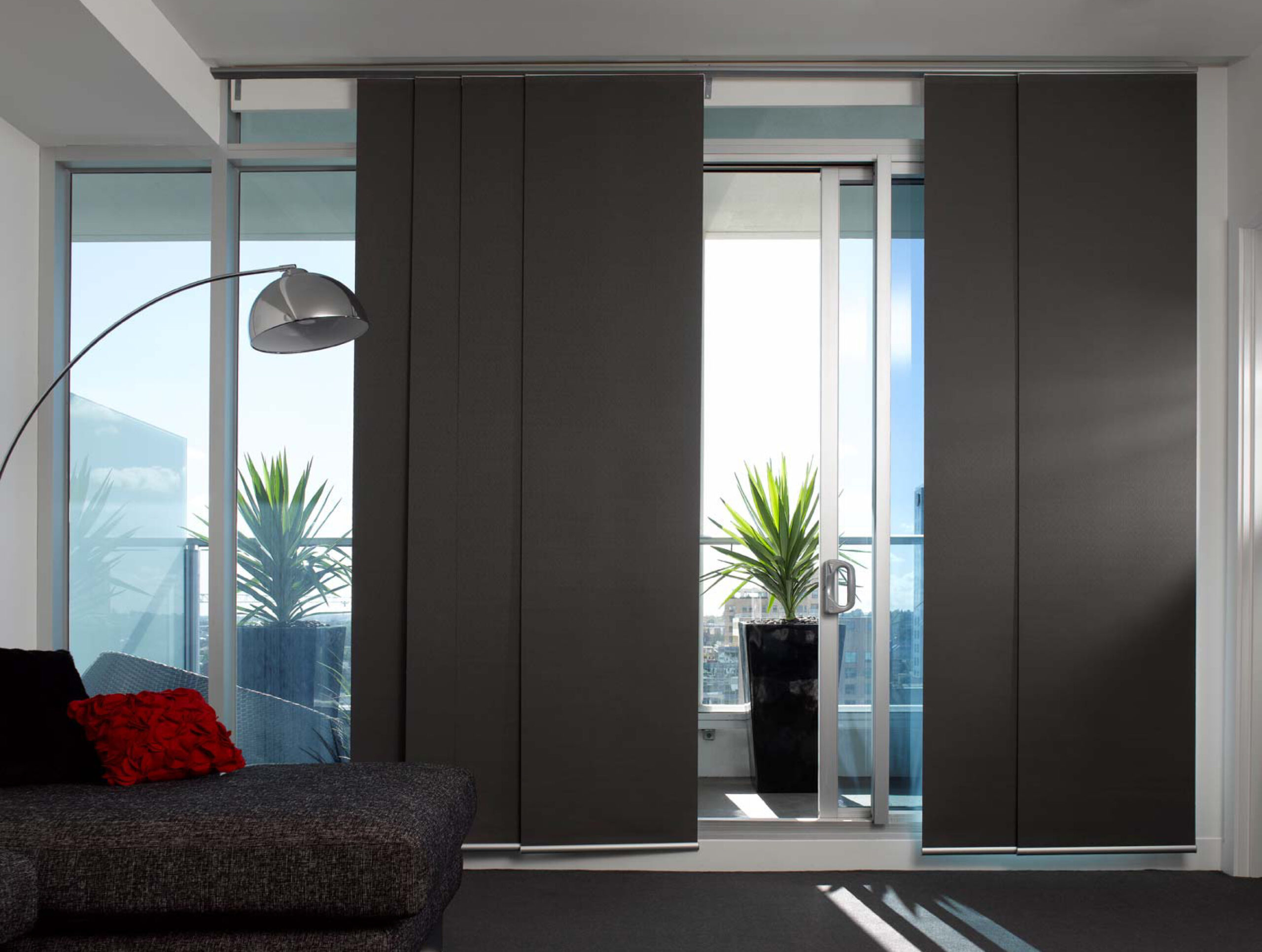 Dark grey panel blinds sliding across floor-to-ceiling windows in a modern apartment lounge